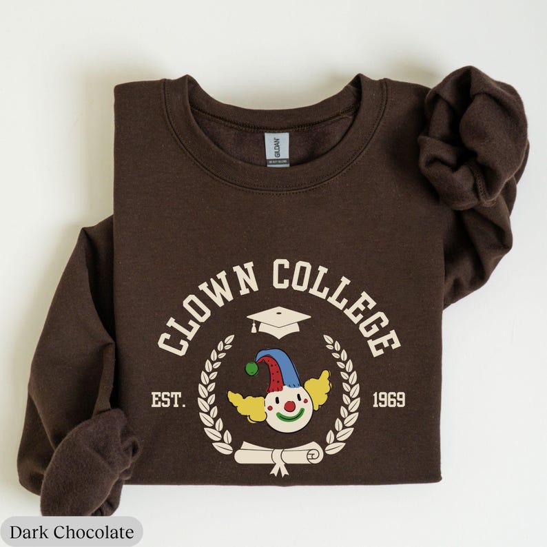 May include: A brown sweatshirt with a white graphic of a clown wearing a graduation cap and holding a diploma. The graphic says "Clown College Est. 1969".