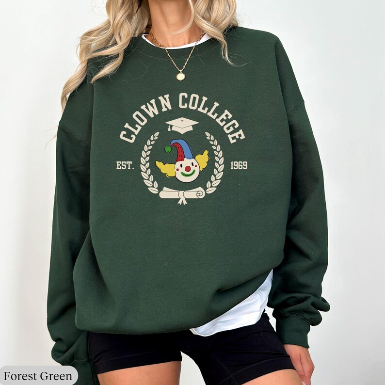 May include: Forest green sweatshirt with the text "Clown College" in white, a graduation cap, and a clown face with the text "Est. 1969".