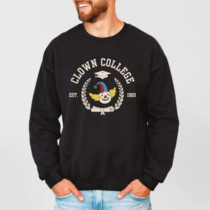 May include: Black sweatshirt with a white graphic of a clown wearing a graduation cap and holding a diploma. The graphic says "Clown College Est. 1969".