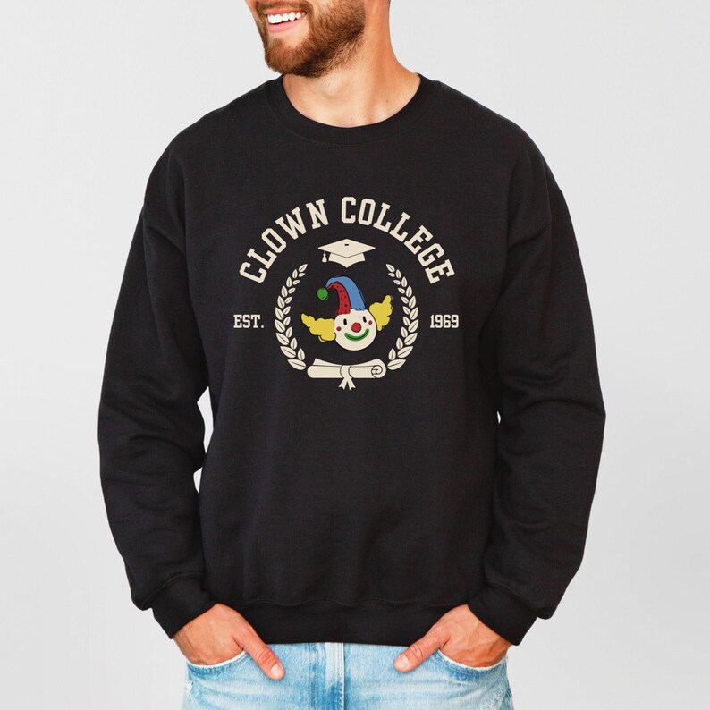 May include: Black sweatshirt with a white graphic of a clown wearing a graduation cap and holding a diploma. The graphic says "Clown College Est. 1969".