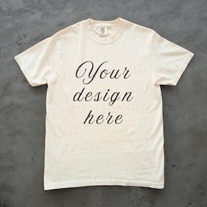 May include: A plain white t-shirt with the text "Your design here" printed in black cursive on the front.