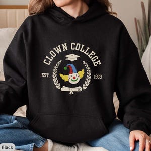 May include: Black hoodie with a white graphic of a clown wearing a graduation cap and holding a diploma. The graphic says "Clown College Est. 1969".
