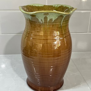 May include: A brown and green ceramic vase with a scalloped rim. The vase has a glazed finish and a subtle ombre effect.