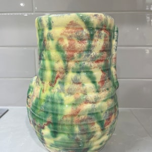 May include: A ceramic vase with a green, yellow and red swirl pattern. The vase has a rounded body and a wide opening.