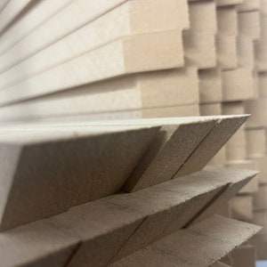May include: Close-up of stacked, unfinished wooden blocks. The blocks are light brown and have a rough, textured surface. The edges are precisely cut, creating a geometric pattern. The image highlights the natural wood grain and the sharp angles of the blocks.