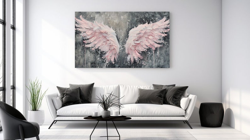 May include: A large, rectangular canvas art piece depicting a pair of pink angel wings against a gray and white textured background. The artwork hangs above a white sofa with black pillows. The room has a modern aesthetic.