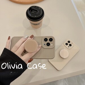 May include: Two beige phone cases with a pop socket on each. The cases have a camera cutout and the text "Olivia Case" is written on the case.