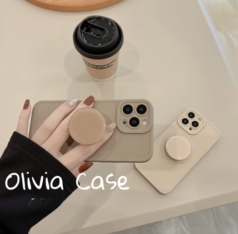 May include: Two beige phone cases with a pop socket on each. The cases have a camera cutout and the text "Olivia Case" is written on the case.