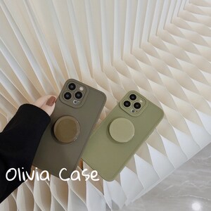 May include: Two green phone cases with a pop socket on the back. The cases are made of a soft, silicone material. The text "Olivia Case" is written on the bottom of the image.