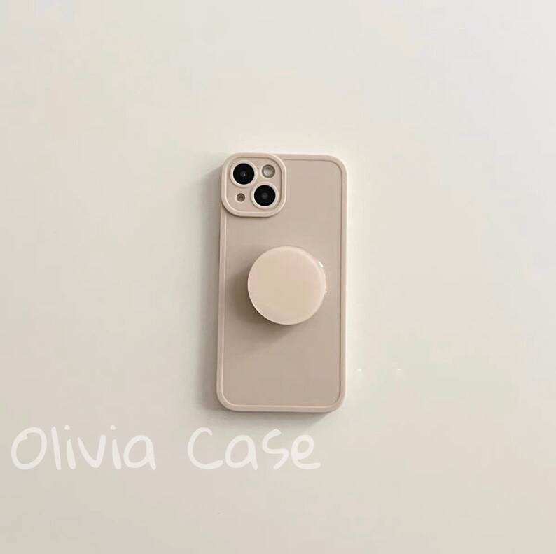 May include: A beige phone case with a pop socket. The case has a camera cutout and the text "Olivia Case" is written below the case.