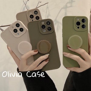 May include: Three phone cases with different colored silicone material. The cases have a raised camera bump and a pop socket on the back. The cases are in the colors beige, green, and brown.