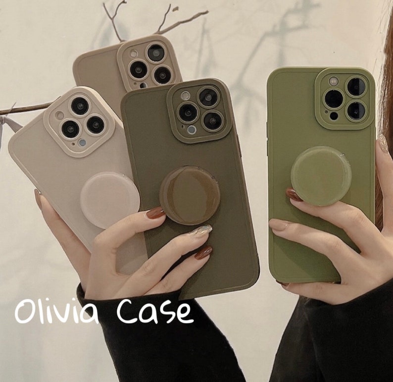 May include: Three phone cases with different colored silicone material. The cases have a raised camera bump and a pop socket on the back. The cases are in the colors beige, green, and brown.