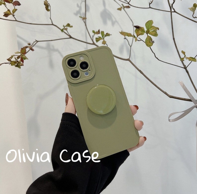 May include: A green phone case with a pop socket. The case has a camera lens cutout and the text "Olivia Case" is printed on the bottom.
