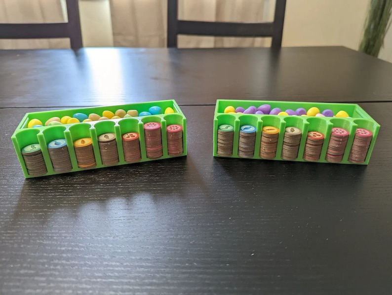 Puede incluir: Dos organizadores de pl&aacute;stico verde con compartimentos para guardar peque&ntilde;as piezas de juego. Cada organizador tiene una fila de huevos de pl&aacute;stico de colores y una pila de piezas de juego marrones, amarillas y verdes.