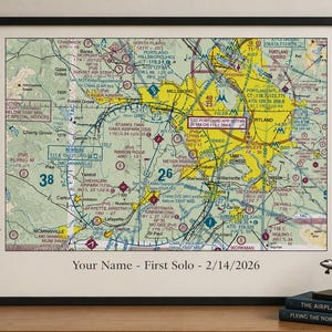 May include: A framed aviation sectional chart of the Portland area featuring yellow and green terrain details, navigation markers, and airspace boundaries. The print includes the text Your Name - First Solo - 2/14/2026 centered at the bottom.