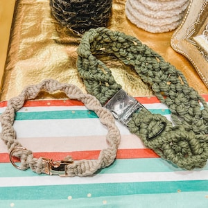 Könnte beinhalten: Zwei handgefertigte Makramee-Hundehalsbänder, eines in hellbraun und eines in dunkelgrün. Beide Halsbänder haben silberne Metallschnallen.