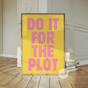 Può includere: Un poster giallo con cornice dorata che presenta il testo "DO IT FOR THE PLOT" in lettere rosa.