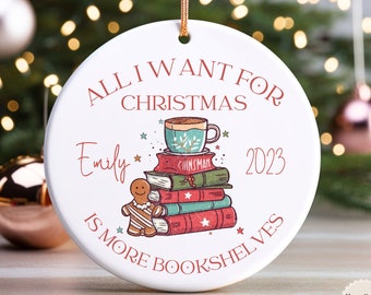 May include: White ceramic Christmas ornament with a red and white gingerbread man, a stack of books, a cup of coffee, and the text "ALL I WANT FOR CHRISTMAS Emily 2023 IS MORE BOOKSHELVES".