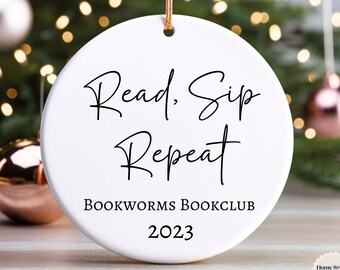 May include: White ceramic Christmas ornament with black text that reads "Read, Sip, Repeat" and "Bookworms Bookclub 2023".