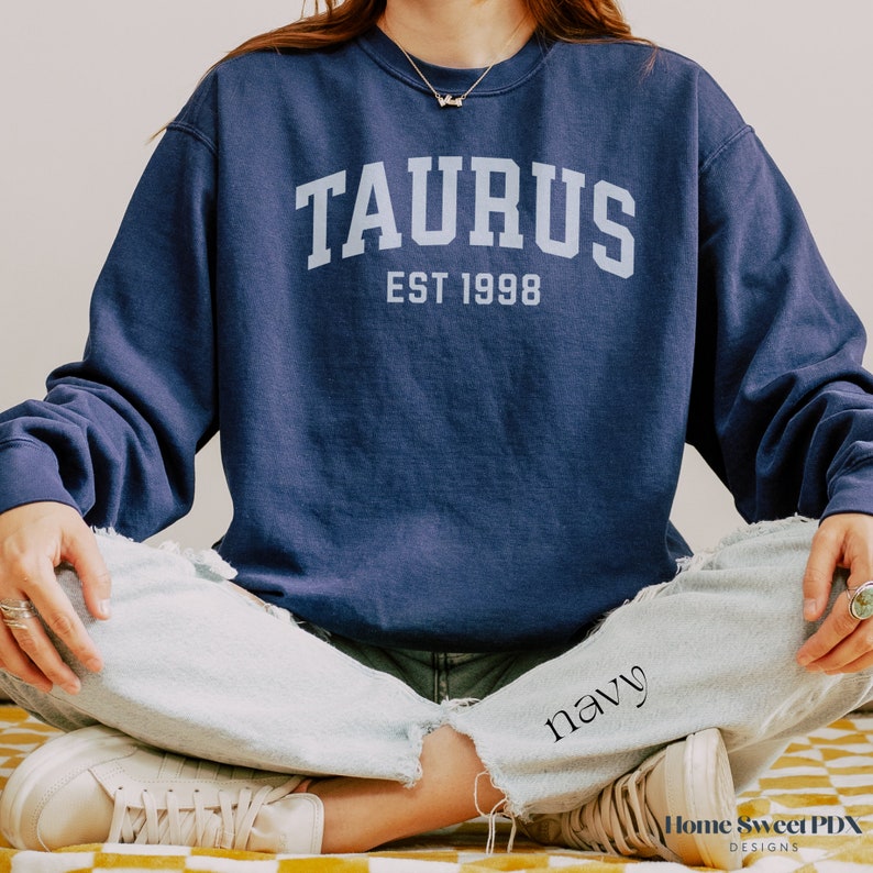 May include: A navy blue sweatshirt with the text "TAURUS EST 1998" in white lettering.