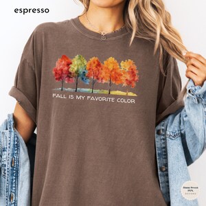May include: A brown t-shirt with a watercolor design of five colorful trees and the text "Fall is my favorite color".