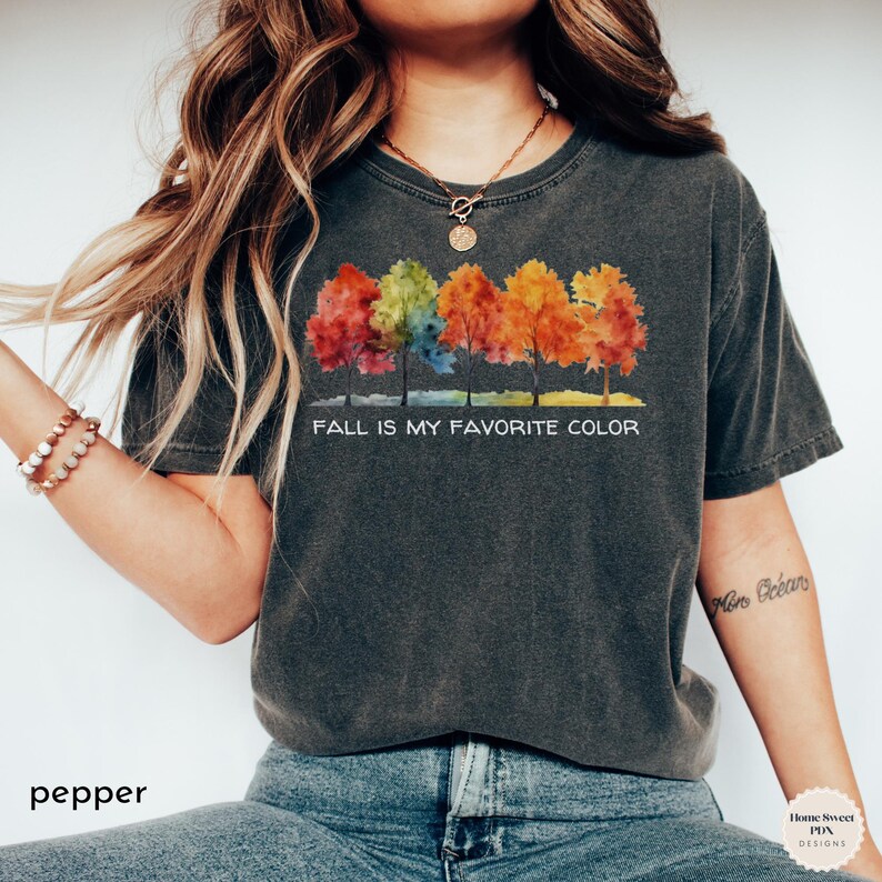May include: A dark gray t-shirt with a watercolor design of colorful trees and the text "Fall is my favorite color".