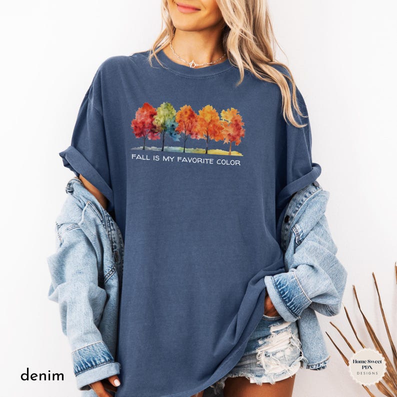 May include: A blue t-shirt with a watercolor design of five trees with fall colors. The text "Fall is my favorite color" is printed below the trees.