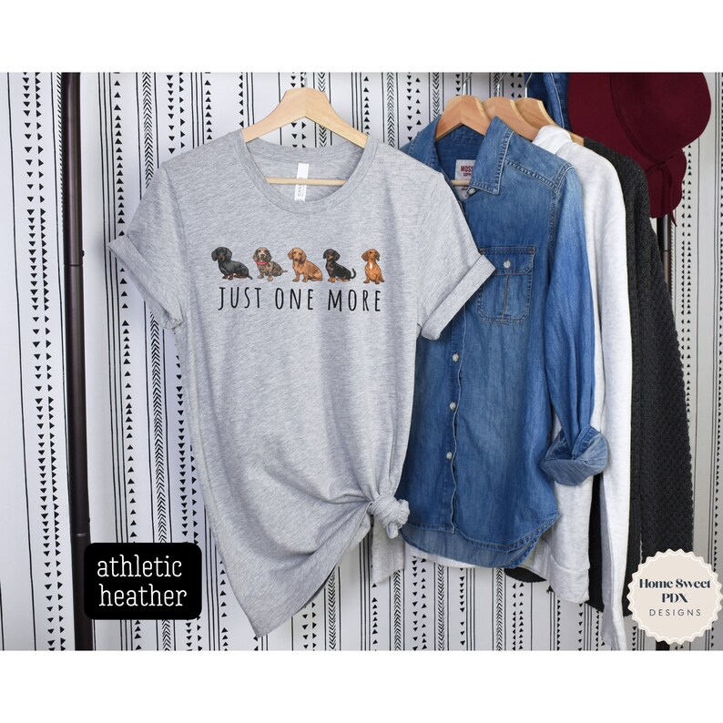 Puede incluir: Una camiseta gris con una l&iacute;nea de perros salchicha y el texto "JUST ONE MORE".