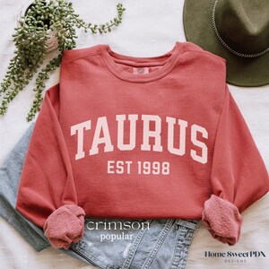 May include: A crimson red sweatshirt with the text "TAURUS EST 1998" in white.