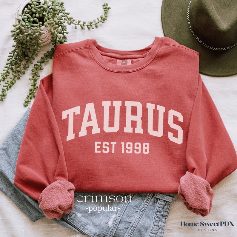 May include: A crimson red sweatshirt with the text "TAURUS EST 1998" in white.