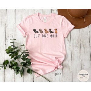Puede incluir: Camiseta rosa con una l&iacute;nea de perros salchicha y el texto "Just One More".