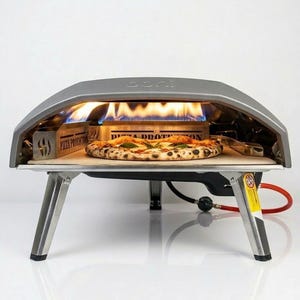 Può includere: Un forno per pizza grigio da esterno con una pizza all'interno, fiamme visibili. Il forno ha un telaio e gambe in acciaio inossidabile. La pizza è su una pala di legno. Il forno ha la scritta "Ooni" sulla parte superiore.