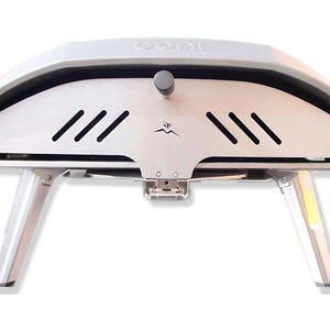 Puede incluir: Un horno de pizza portátil plateado y gris con un soporte plegable. El horno tiene una pequeña puerta con una perilla negra y un logotipo que dice "Ooni" en la parte superior. El horno tiene un interior de acero inoxidable con una ventilación y un logotipo con una cordillera y una llama.