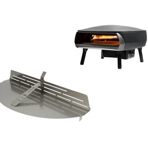 Könnte beinhalten: Ein schwarzer Pizzaofen mit einer Pizzenschaufel aus Edelstahl. Der Ofen hat eine runde Öffnung und steht auf vier Beinen. Die Schaufel ist halbkreisförmig und hat einen Griff.