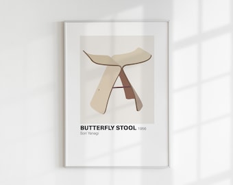 May include: A framed print of a white butterfly stool with brown legs. The print includes the text "BUTTERFLY STOOL 1956 Sori Yanagi".