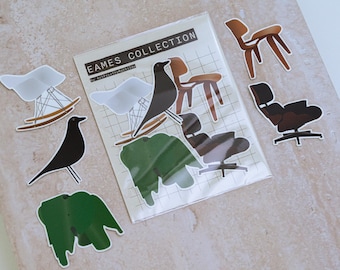 May include: A collection of stickers featuring Eames chairs, a black bird, and green leaf shapes. The stickers are in a clear plastic sleeve with the text "EAMES COLLECTION". The stickers are on a light beige surface.