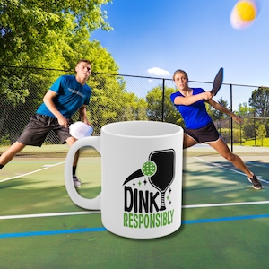 A man & women play pickleball and a white coffee mug with Dink Responsibly funny Pickleball slogan on it in superimposed on the court.