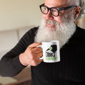 Middle aged man holds a white coffee mug with Dink Responsibly funny Pickleball slogan on it.