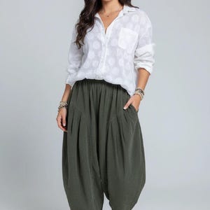 Pode incluir: Uma camisa branca de manga comprida com bot&otilde;es, um padr&atilde;o subtil de bolinhas e um bolso no peito, combinada com cal&ccedil;as largas verde-azeitona com cintura el&aacute;stica, bolsos laterais profundos e bainha afunilada, usada com t&eacute;nis brancos.