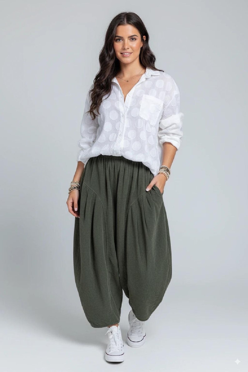 Pode incluir: Uma camisa branca de manga comprida com bot&otilde;es, um padr&atilde;o subtil de bolinhas e um bolso no peito, combinada com cal&ccedil;as largas verde-azeitona com cintura el&aacute;stica, bolsos laterais profundos e bainha afunilada, usada com t&eacute;nis brancos.