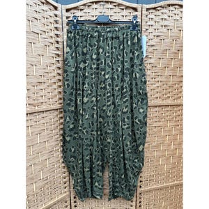 May include: Olive green harem trousers featuring a dark black leopard print pattern throughout. The trousers have a wide, loose-fitting silhouette with a gathered elastic waistband and are displayed on a black plastic hanger for clear visibility.