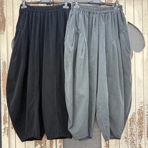 Pode incluir: Dois pares de cal&ccedil;as de corte largo pendurados em cabides de pl&aacute;stico preto. Um par &eacute; preto s&oacute;lido e o outro &eacute; de um cinzento escuro suave. Ambos apresentam cintura el&aacute;stica, bolsos laterais profundos e uma silhueta de perna arredondada.