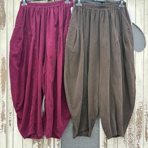 Pode incluir: Dois pares de cal&ccedil;as largas com cintura el&aacute;stica. Um par &eacute; de cor bord&ocirc; escuro e o outro &eacute; de cor castanho escuro. Ambos apresentam uma silhueta volumosa e franzida com bolsos laterais e uma bainha afunilada nos tornozelos.