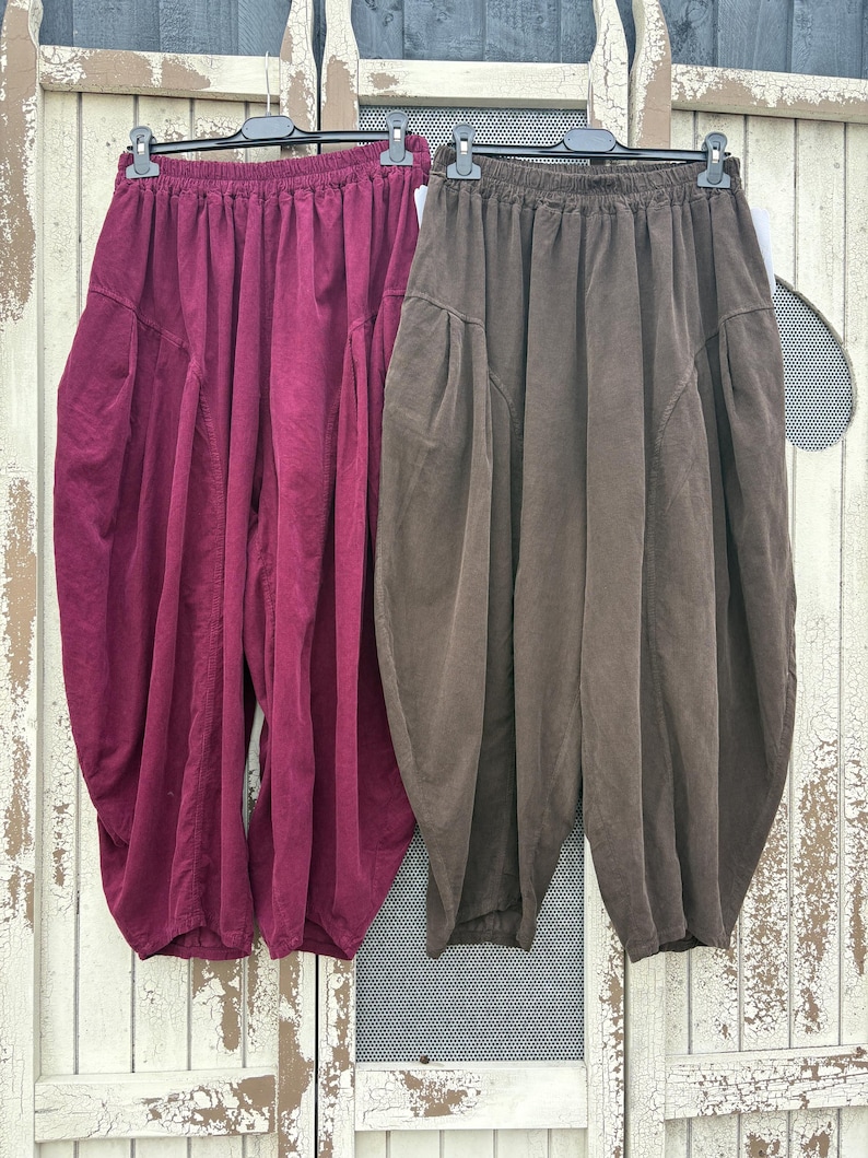 Pode incluir: Dois pares de cal&ccedil;as largas com cintura el&aacute;stica. Um par &eacute; de cor bord&ocirc; escuro e o outro &eacute; de cor castanho escuro. Ambos apresentam uma silhueta volumosa e franzida com bolsos laterais e uma bainha afunilada nos tornozelos.