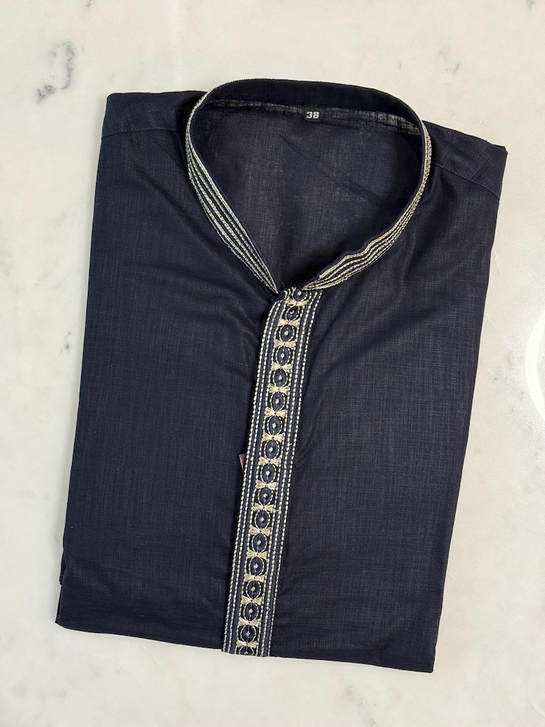 May include: Navy blue kurta shirt with a mandarin collar and decorative trim. The trim features a gold and silver pattern with circular accents. The shirt is folded neatly, showing the front and collar details. The number "38" is visible on the collar.