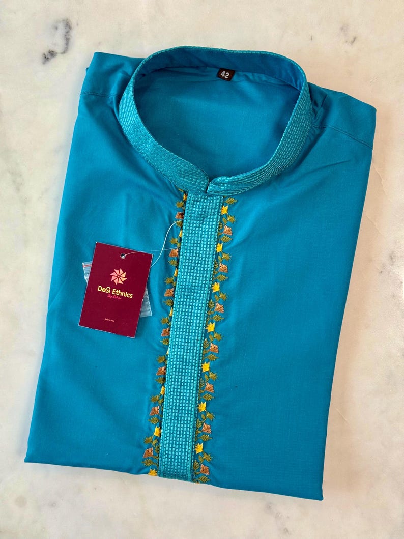 May include: A turquoise kurta shirt with a mandarin collar and embroidered detailing. The shirt features a vertical embroidered panel with floral accents. A tag from "DeSi Ethnics" is attached. The size tag reads "42".