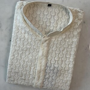 Pu&ograve; includere: Camicia kurta ricamata color crema con colletto alla coreana. La camicia presenta un motivo floreale all-over e una chiusura con bottoni. Il tessuto sembra leggero, adatto alle temperature calde. La camicia &egrave; piegata ordinatamente, mostrando i dettagli del ricamo.