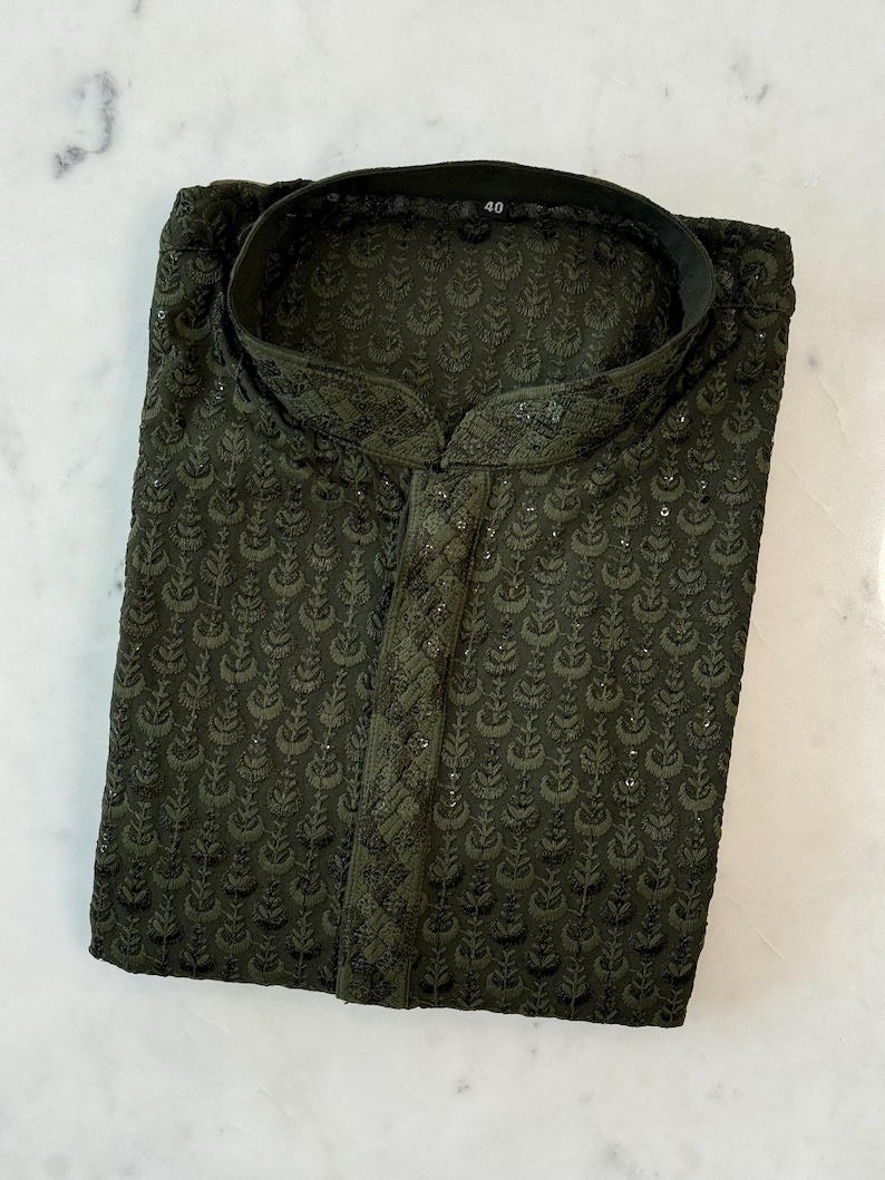 Pu&ograve; includere: Kurta ricamata verde scuro con colletto alla coreana. La camicia a maniche lunghe presenta un motivo floreale all-over e una chiusura con bottoni sul davanti. L'etichetta della taglia indica "40". L'indumento &egrave; piegato ordinatamente su una superficie bianca.