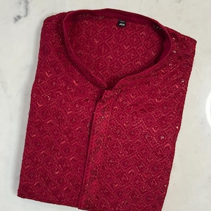 Pu&ograve; includere: Una camicia rosso scuro a maniche lunghe con intricati dettagli ricamati. Presenta un colletto alla coreana e una chiusura frontale con bottoni. Il tessuto ha una leggera lucentezza e il design suggerisce un capo formale o festivo. Taglia 42.