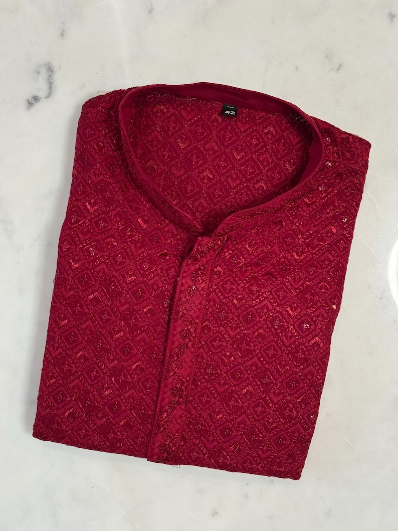 Pu&ograve; includere: Una camicia rosso scuro a maniche lunghe con intricati dettagli ricamati. Presenta un colletto alla coreana e una chiusura frontale con bottoni. Il tessuto ha una leggera lucentezza e il design suggerisce un capo formale o festivo. Taglia 42.